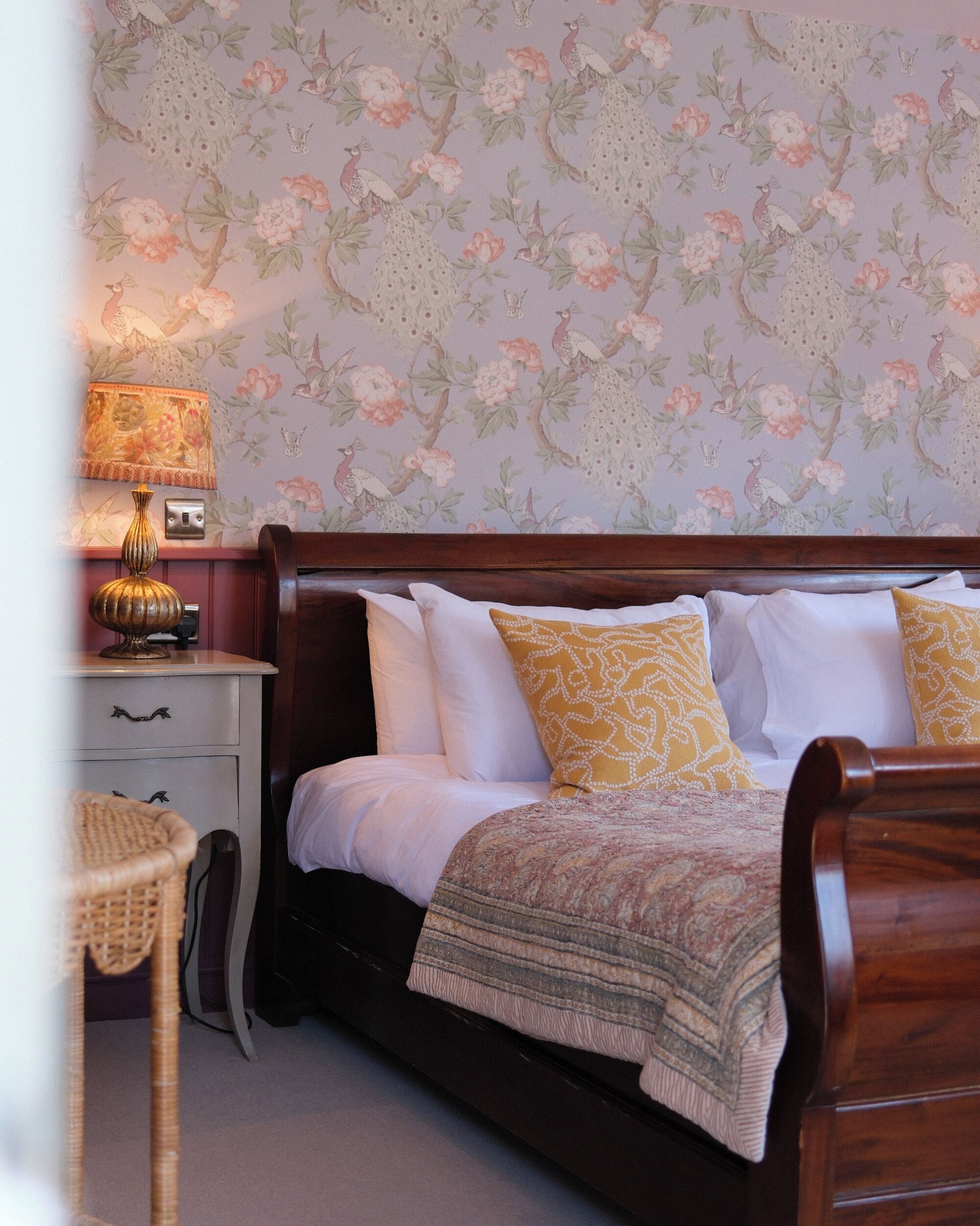 A bedroom with a bed, nightstand, lamp, and a chair.