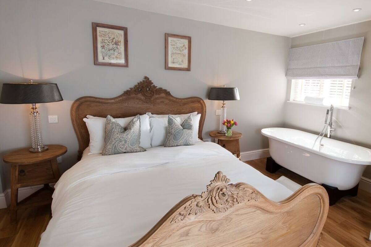 Un dormitorio con una cama grande, dos lámparas de noche, un cabecero de madera, un baño blanco y una ventana con persianas.