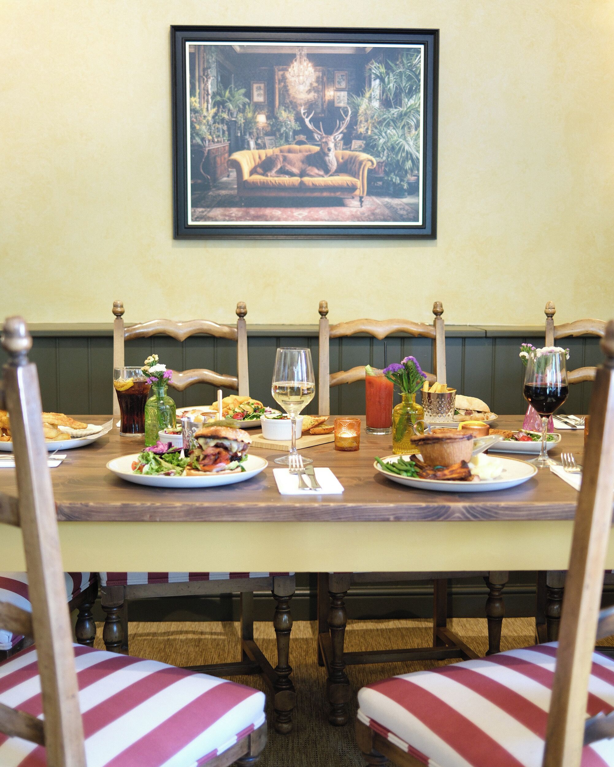 A dining table set with plates, glasses, and a variety of food items, surrounded by upholstered chairs with striped cushions.