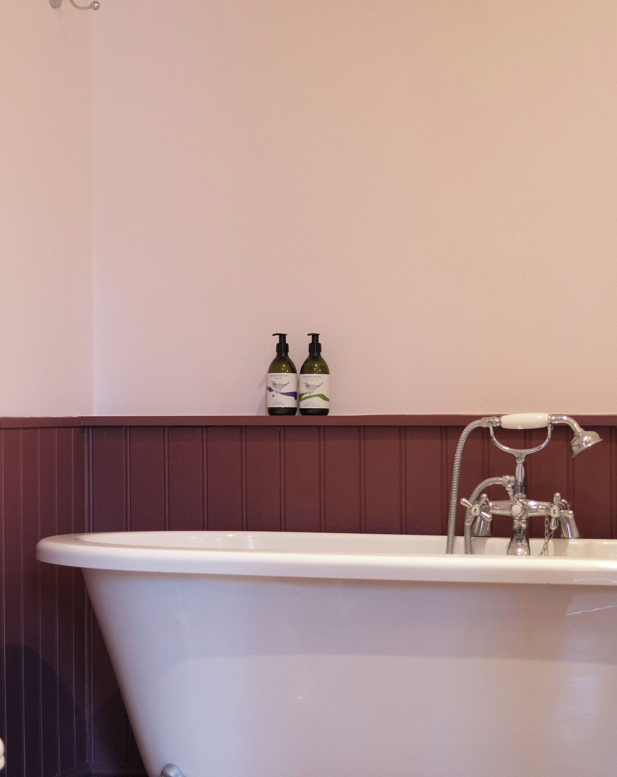 A bathroom with a freestanding bathtub, a wall-mounted shelf with two bottles, and a vintage-style faucet.