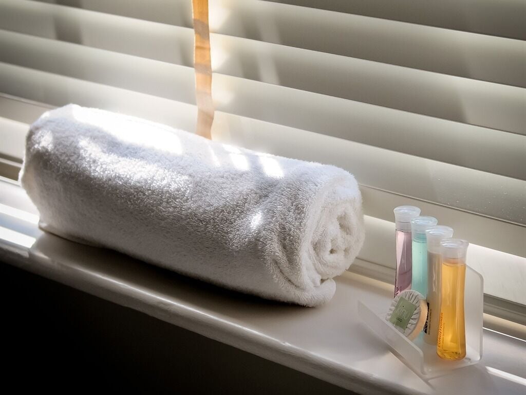 A rolled white towel on a window sill next to a tray with bottles of bath products.