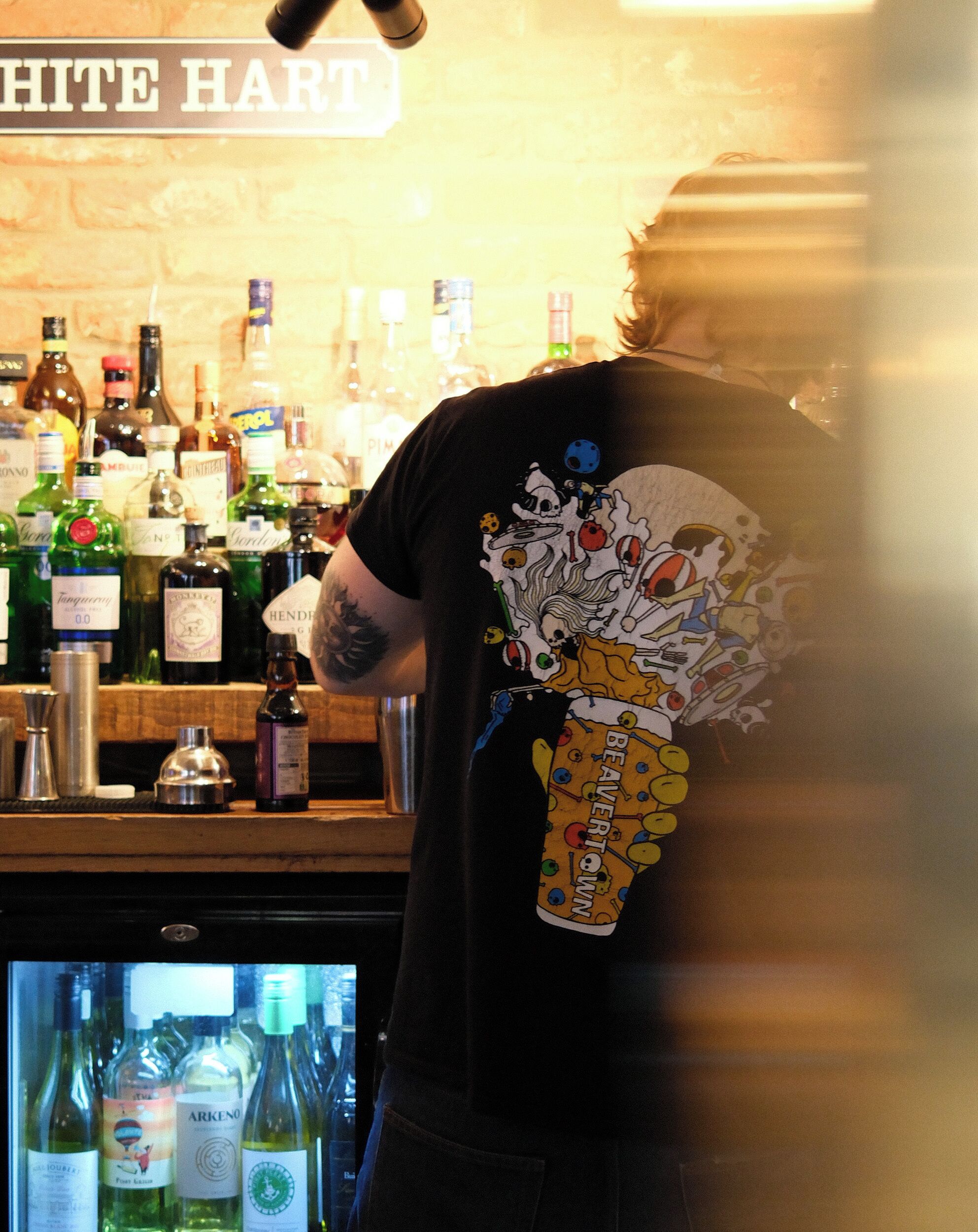 Un coin bar avec différentes bouteilles et une personne portant un t-shirt à motifs.