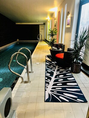 An indoor swimming pool with a lounge area, including a sofa and potted plants. - Dome House (Windermere)