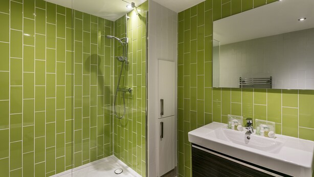 A bathroom with green tiled walls, a white sink, and a glass-enclosed shower. - Dome House (Windermere)