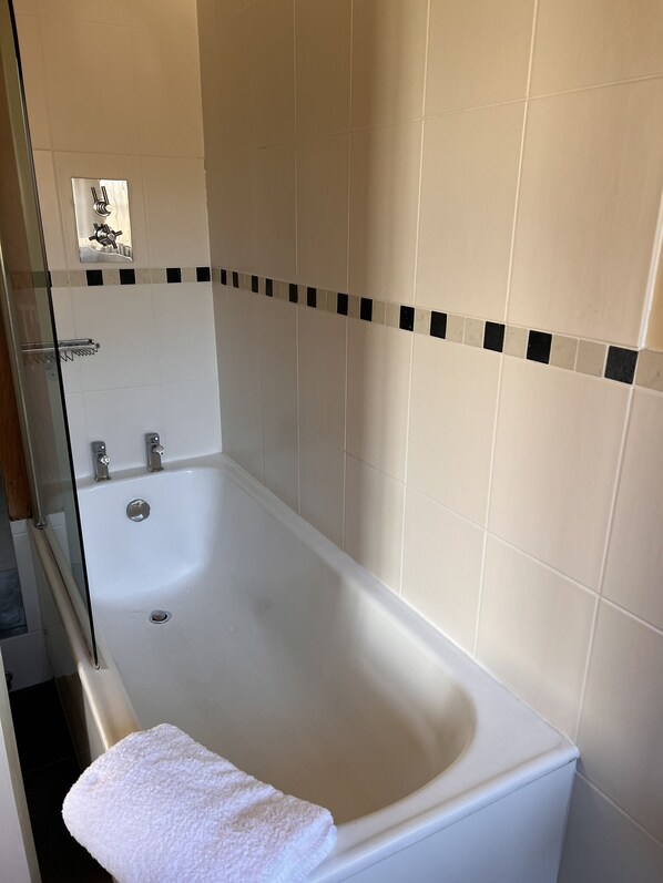 A bathroom with a bathtub, a glass shower enclosure, and a towel.