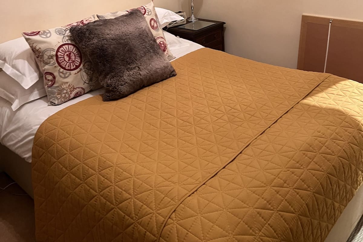 Una cama con cubrecolcha acolchada, una almohada, una lámpara de noche y un cuadro en la pared.