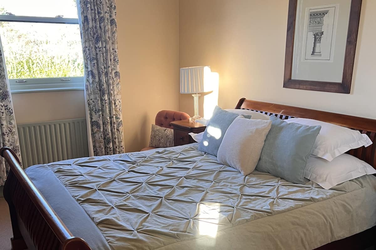Una cama con cubierta acolchada, una mesita de noche con lámpara, una silla y un cuadro en la pared.