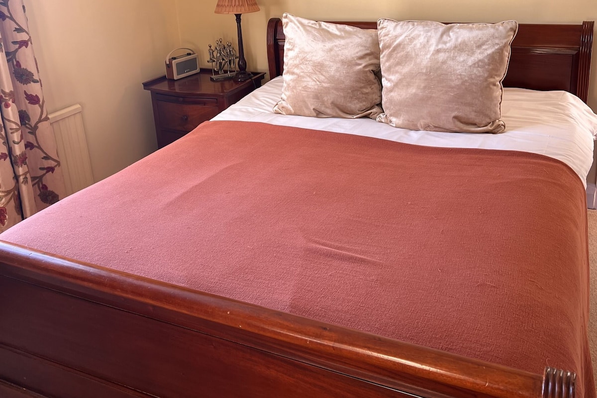 Una cama con estructura de madera, una colcha roja y dos almohadas.