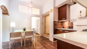 A modern kitchen with wooden cabinets, a white countertop, and a dining area with a table and chairs.