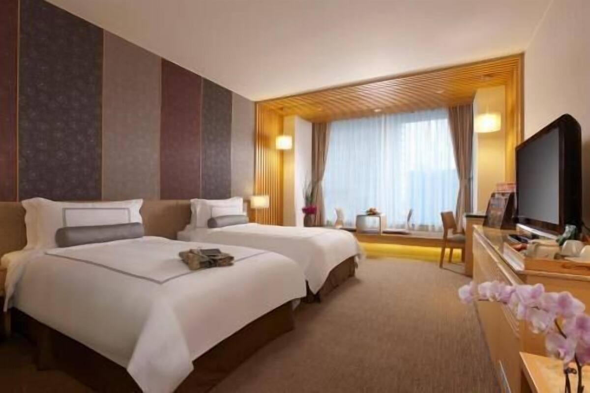 Ett hotellrum med två sängar, en tv, ett skrivbord med en dator och ett fönster med gardiner.