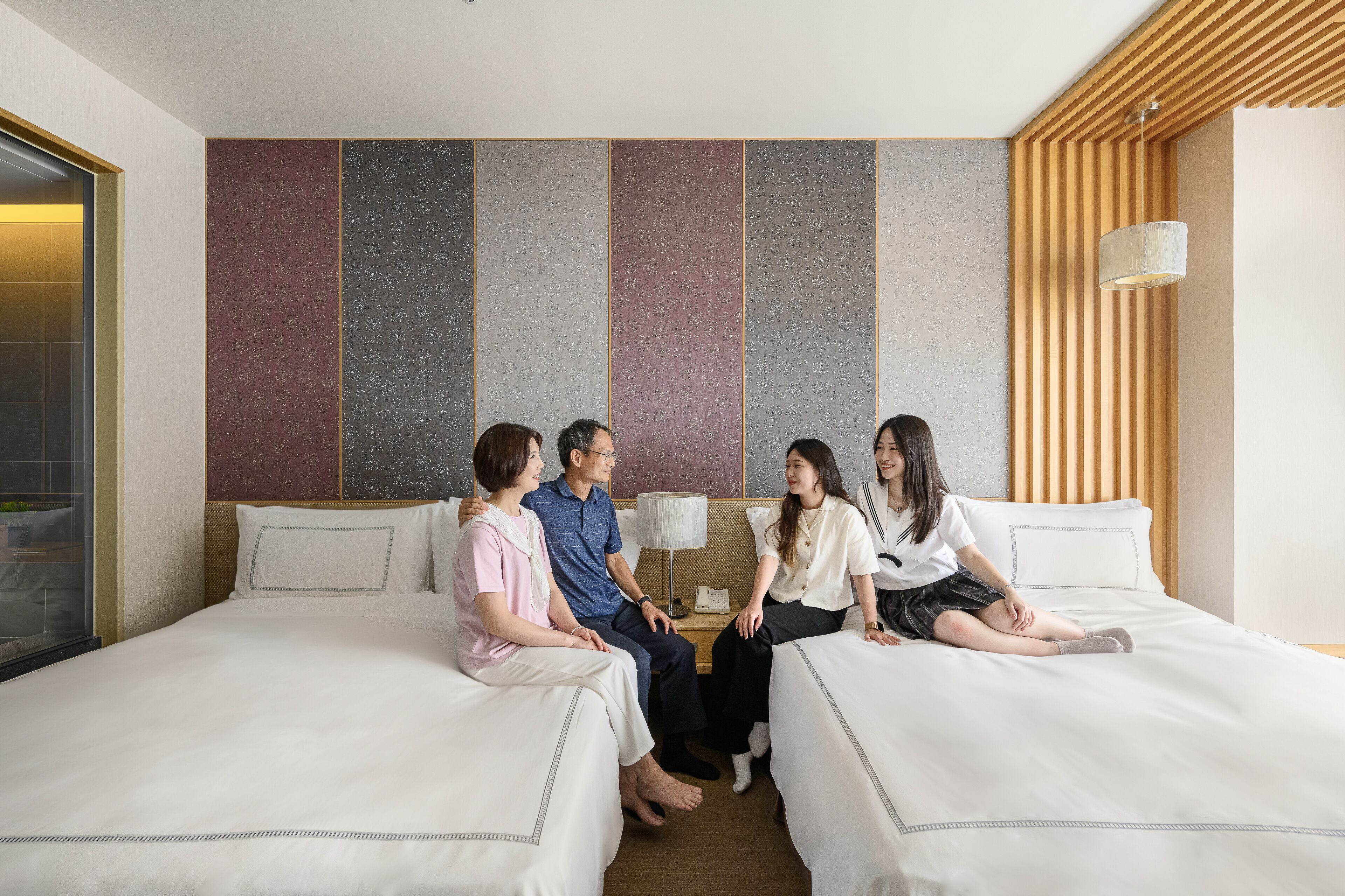 A hotel room with two beds, a large window, and a wooden slat wall design.