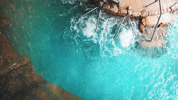 A pool with a stone edge and a metal ladder.