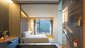 A hotel room with a bed, a bathroom with a towel rack, a plant, and a view of a mountain.