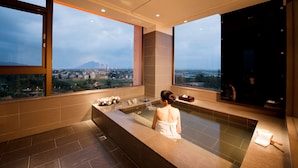 A modern bathroom with a large bathtub, a vanity with a mirror, and a view of a cityscape and a mountain.