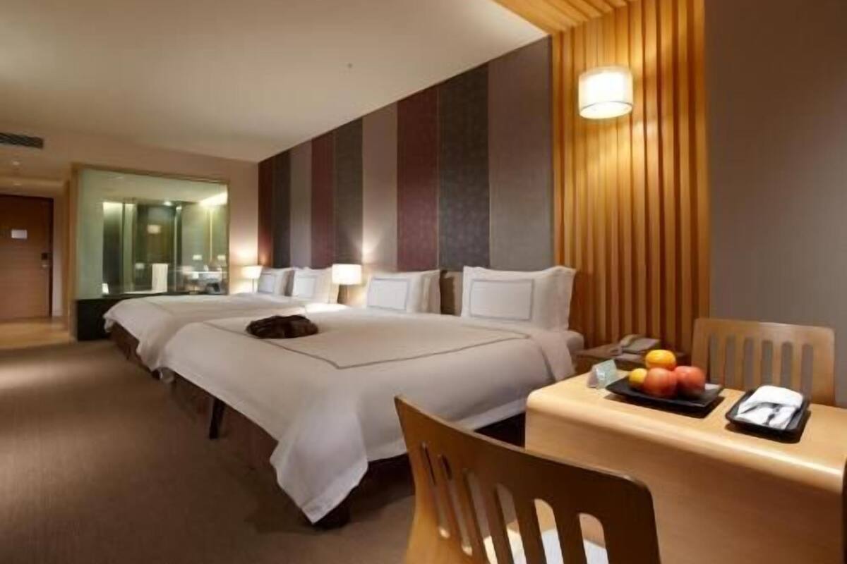 Ett hotellrum med två sängar, ett matbord med frukt, en spegel och en väggpanel i trä.