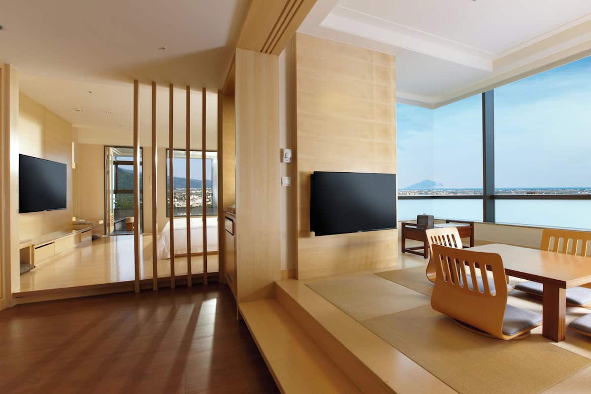 Ett modernt hotellrum med en stor TV, möbler i trä och utsikt över staden.