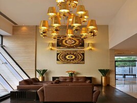 A modern lobby with a large chandelier, two sofas, and a decorative wall piece.