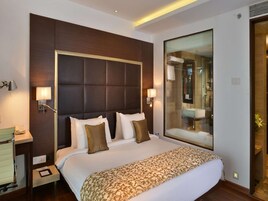 A hotel room with a large bed, a bedside table with a lamp, a mirror, and a view of the bathroom.