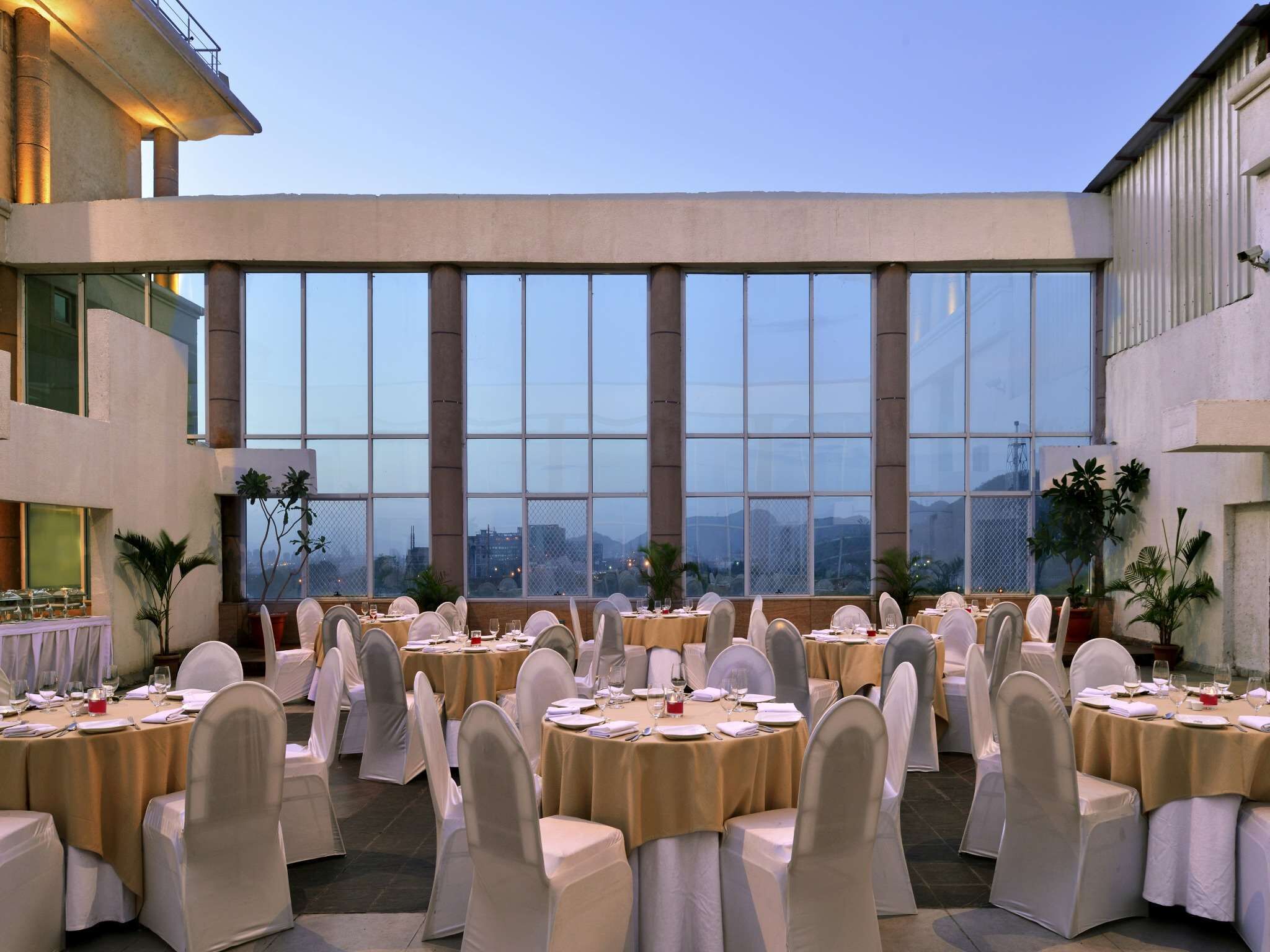 A banquet hall with round tables set for a formal event, large windows offering a city view, and a modern architectural style.