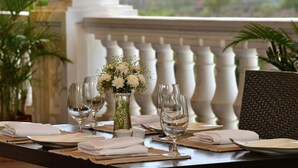 A dining table set with white plates, glasses, and a vase of flowers, overlooking a cityscape. - Majestic Court Sarovar Portico Navi Mumbai (Navi Mumbai)