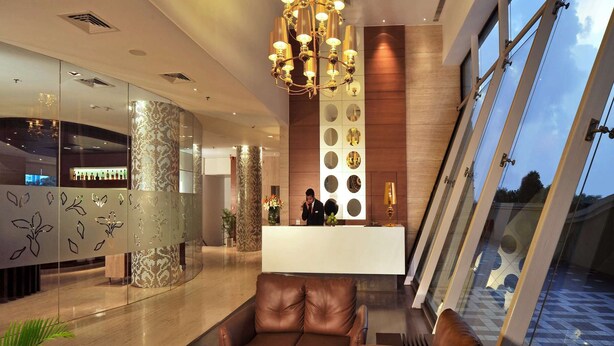 A modern lobby with a reception desk, leather seating, a chandelier, and large windows. - Majestic Court Sarovar Portico Navi Mumbai (Navi Mumbai)