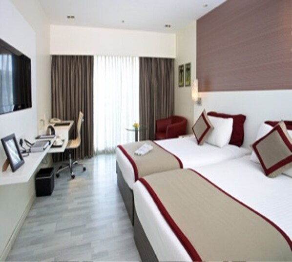 A hotel room with two beds, a desk, a chair, and a TV.