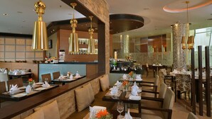 A restaurant with multiple dining tables set for guests, a bar area with bottles, and a modern interior design. - Majestic Court Sarovar Portico Navi Mumbai (Navi Mumbai)