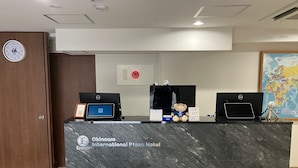 A reception desk with two laptops, a teddy bear, and a map on the wall. - Enagic Okinawa International Plaza Hotel (Naha)
