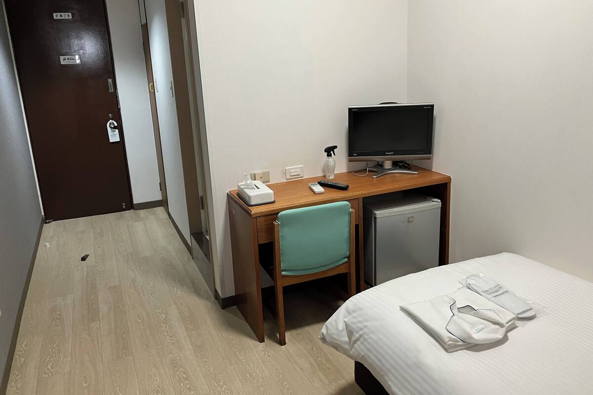 Une chambre d’hôtel équipée d’un lit, d’un bureau avec un ordinateur, d’une chaise et d’un petit réfrigérateur.