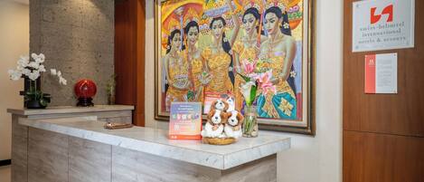 A reception desk with a large painting, a framed menu, and a sign for Swiss-Belhotel International Hotels & Resorts.