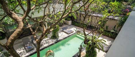 Área de piscina no terraço com espreguiçadeiras e uma pequena estátua, cercada por vegetação e um céu limpo.