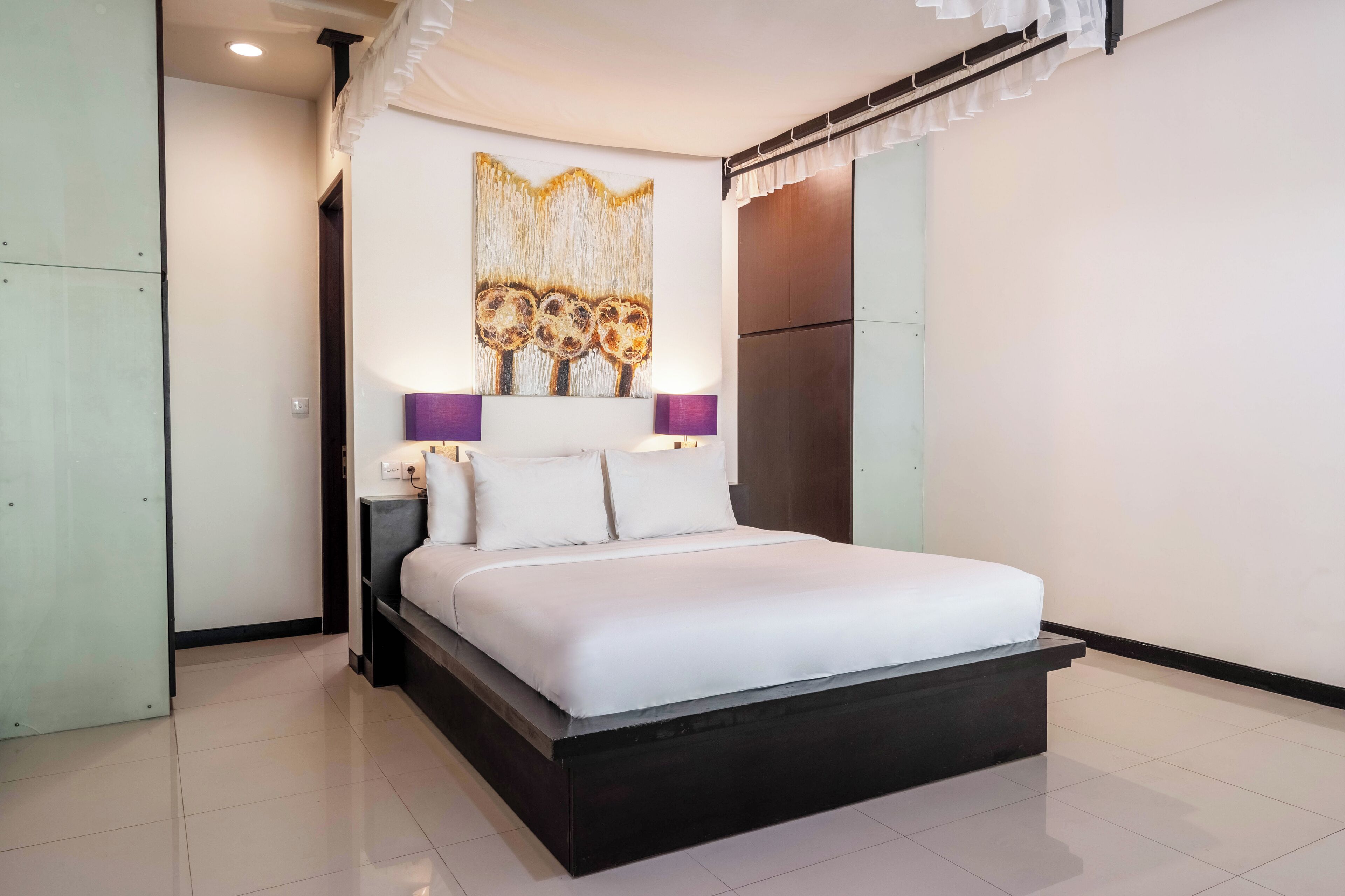 Quarto moderno com cama grande, uma obra de arte na parede e mesa de cabeceira com abajur.