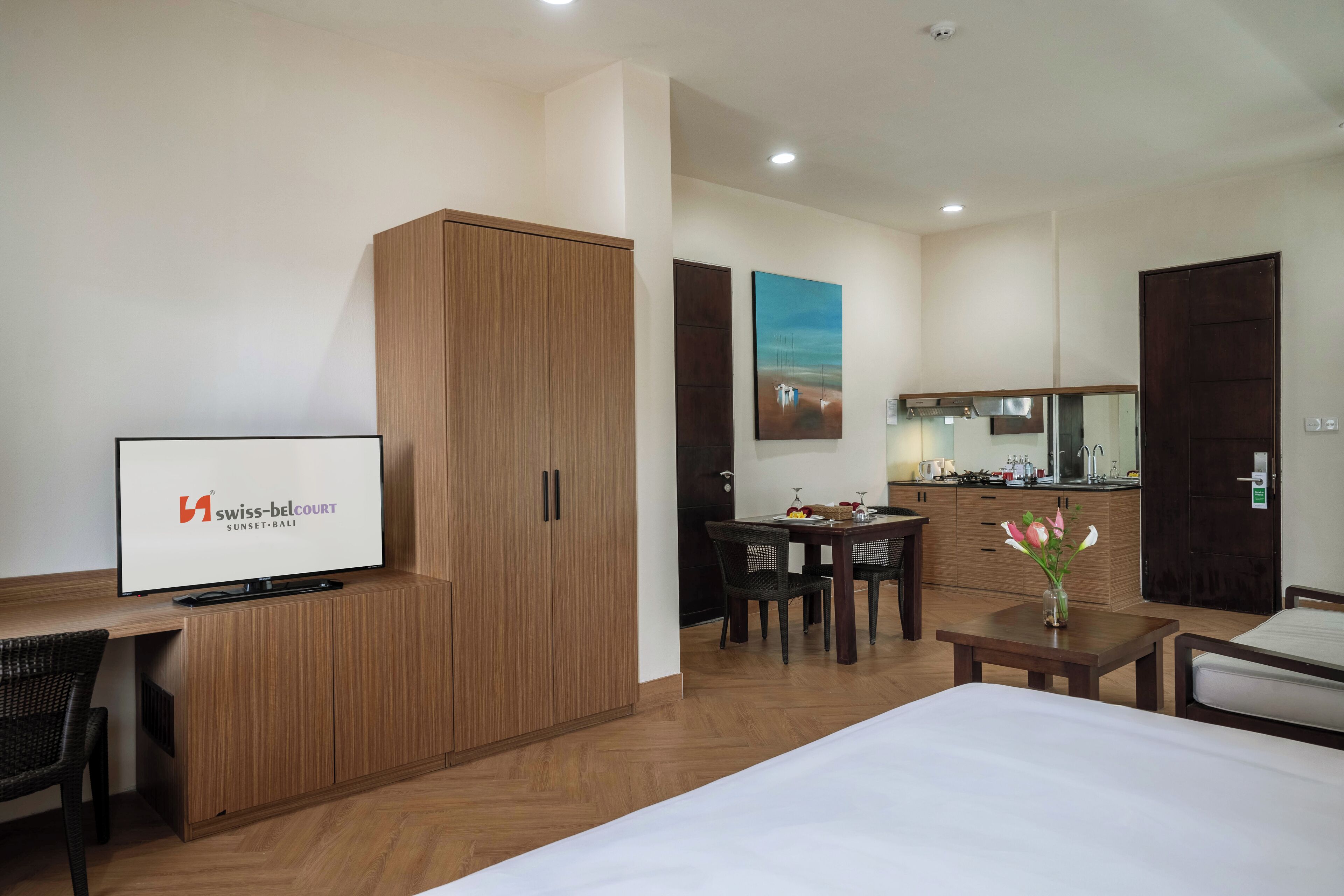 A hotel room with a bed, a desk, a wardrobe, a dining area, and a kitchen.