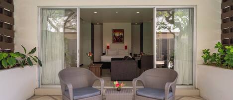 A balcony with wicker chairs, a small table, and a bed in the background.