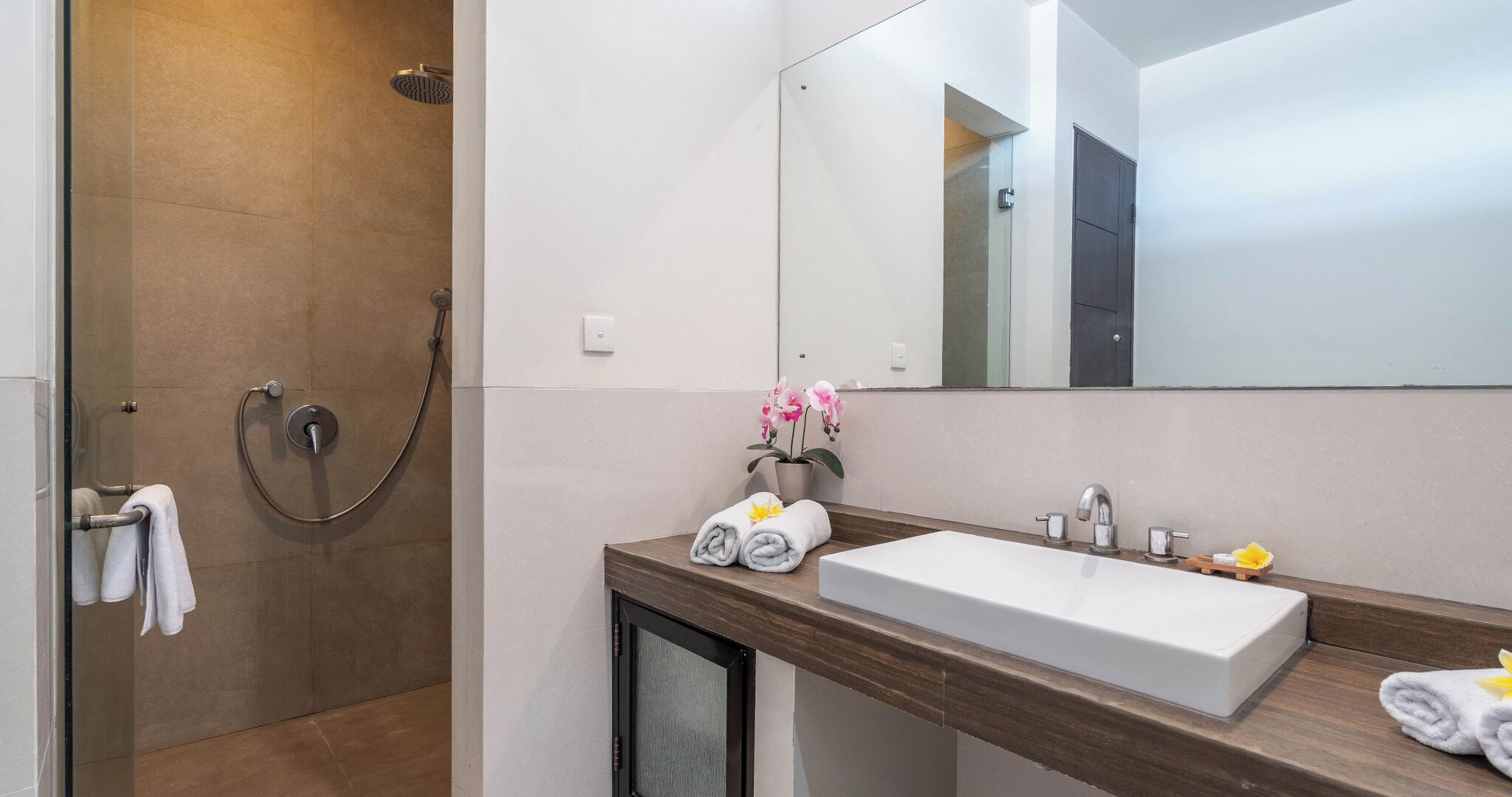A modern bathroom with a walk-in shower, a large mirror, and a wooden vanity with a white sink.