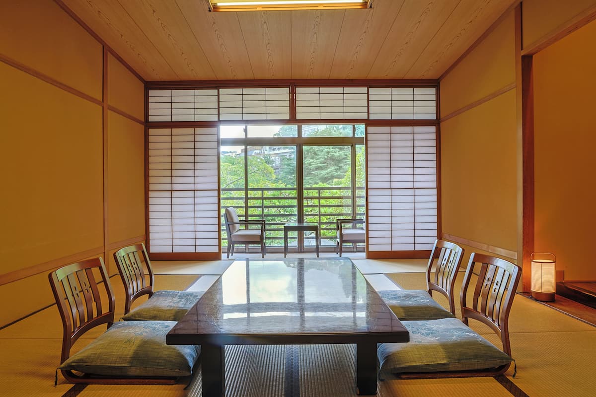 A traditional Japanese room with tatami flooring, a low table, and wooden chairs.