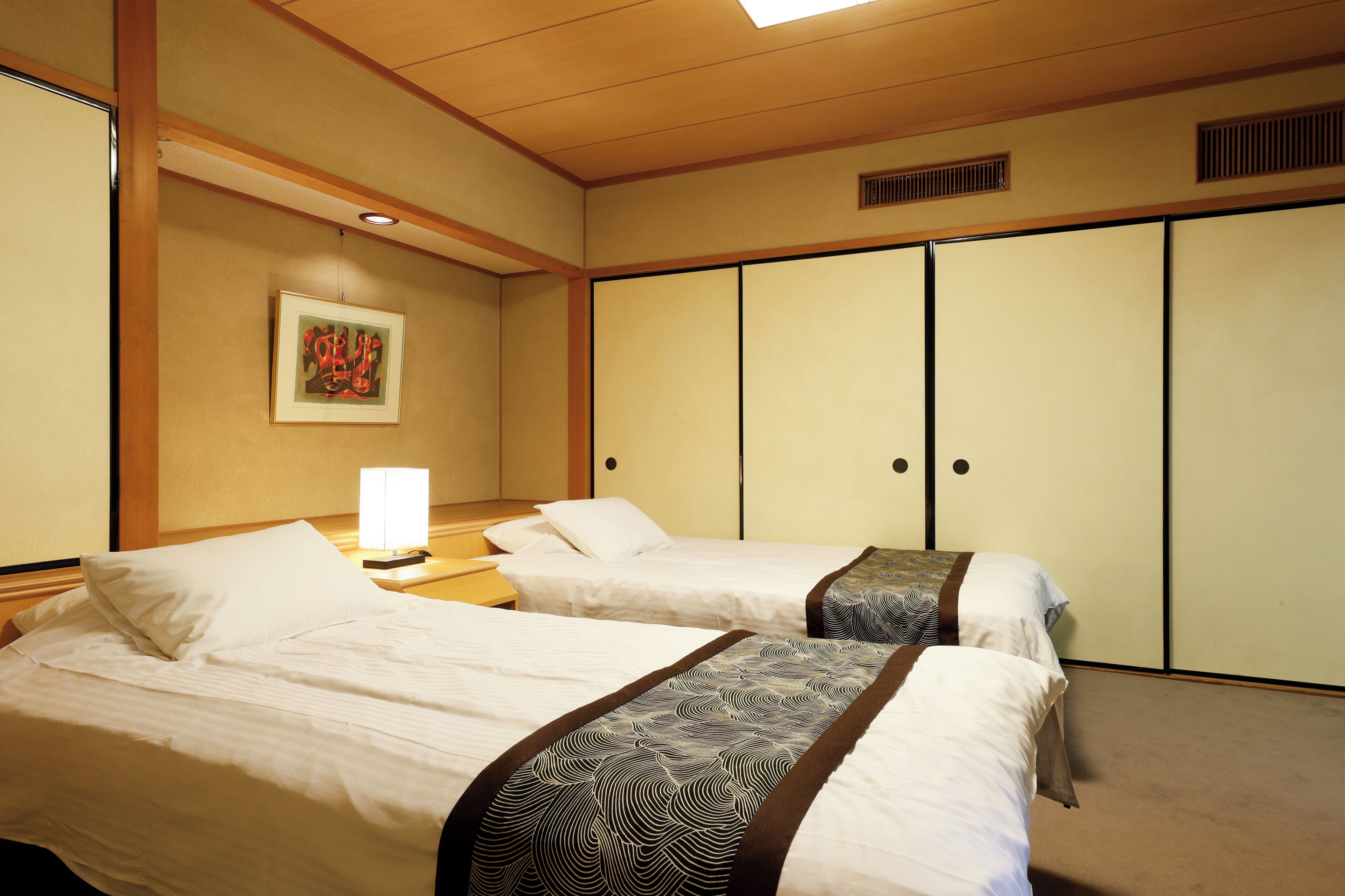A hotel room with two beds, a nightstand, a lamp, a painting on the wall, and a wardrobe.