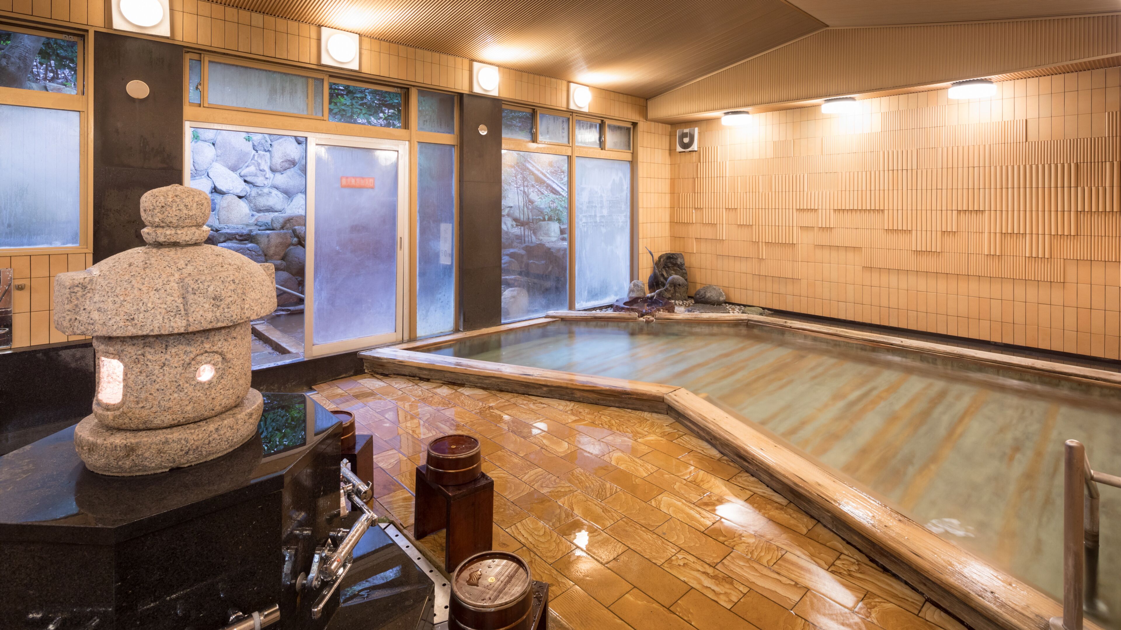 Un onsen japonais traditionnel, agrémenté d’une sculpture en pierre, d’un plancher en bois et d’une grande source d’eau chaude.