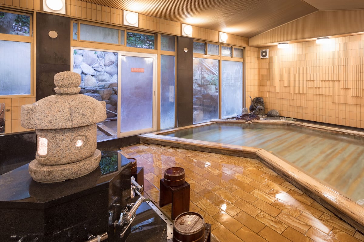 A traditional Japanese onsen with a stone sculpture, wooden flooring, and a large hot spring.