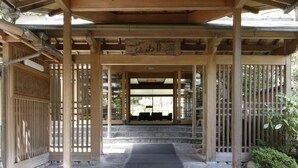 Un pabellón japonés tradicional con estructura de madera, escalones de piedra y un felpudo negro en la entrada.