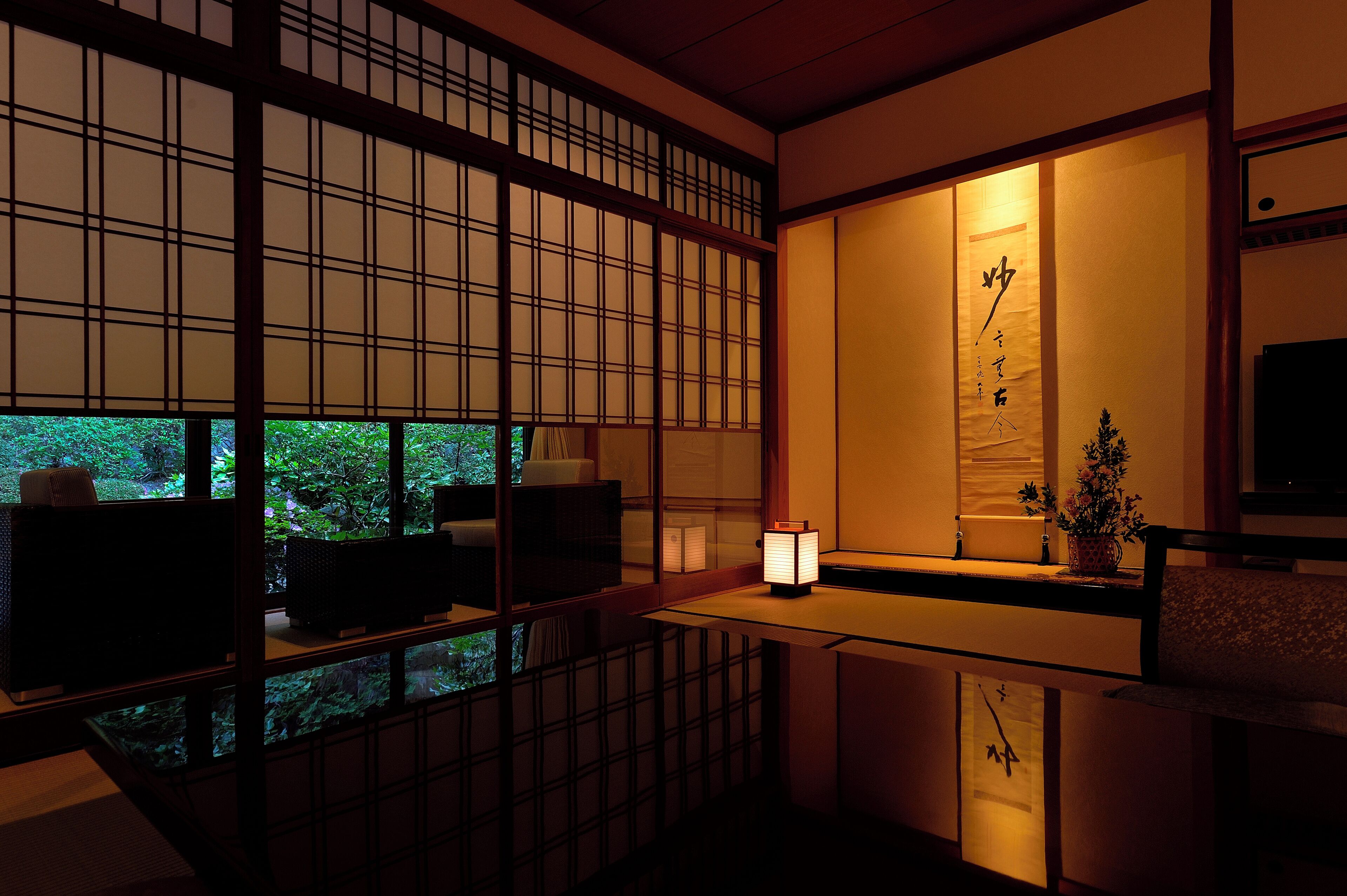 A traditional Japanese room with tatami flooring, a low table, and a sliding door with a view of greenery outside.