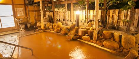 A traditional Japanese onsen with a wooden structure, stone seating, and a large hot spring pool.