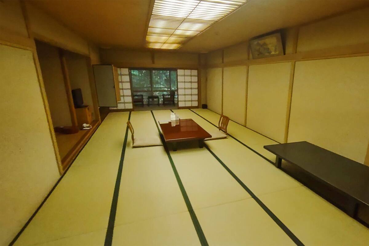 A tatami mat room with a low table, a bench, and a TV on a stand.