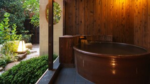 Un espacio de spa de madera con un jacuzzi, techo de madera y un jardín con plantas y una lámpara.