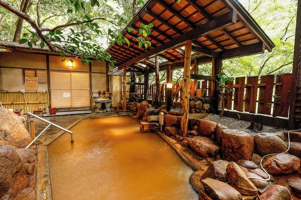 Un onsen japonés tradicional con estructura de madera, un baño de aguas termales y una cerca de madera.