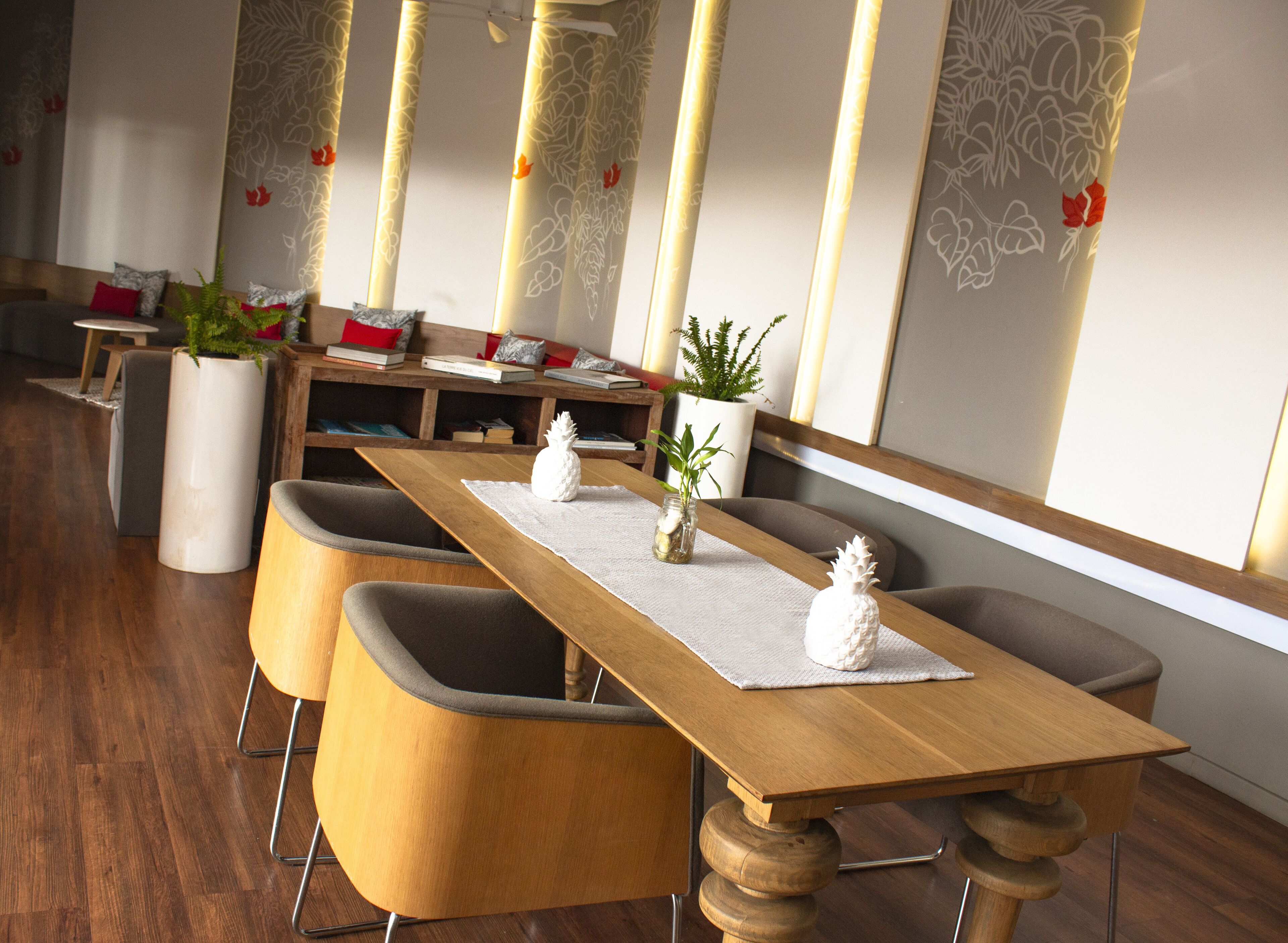 A modern dining area with wooden tables and chairs, potted plants, and books on shelves.
