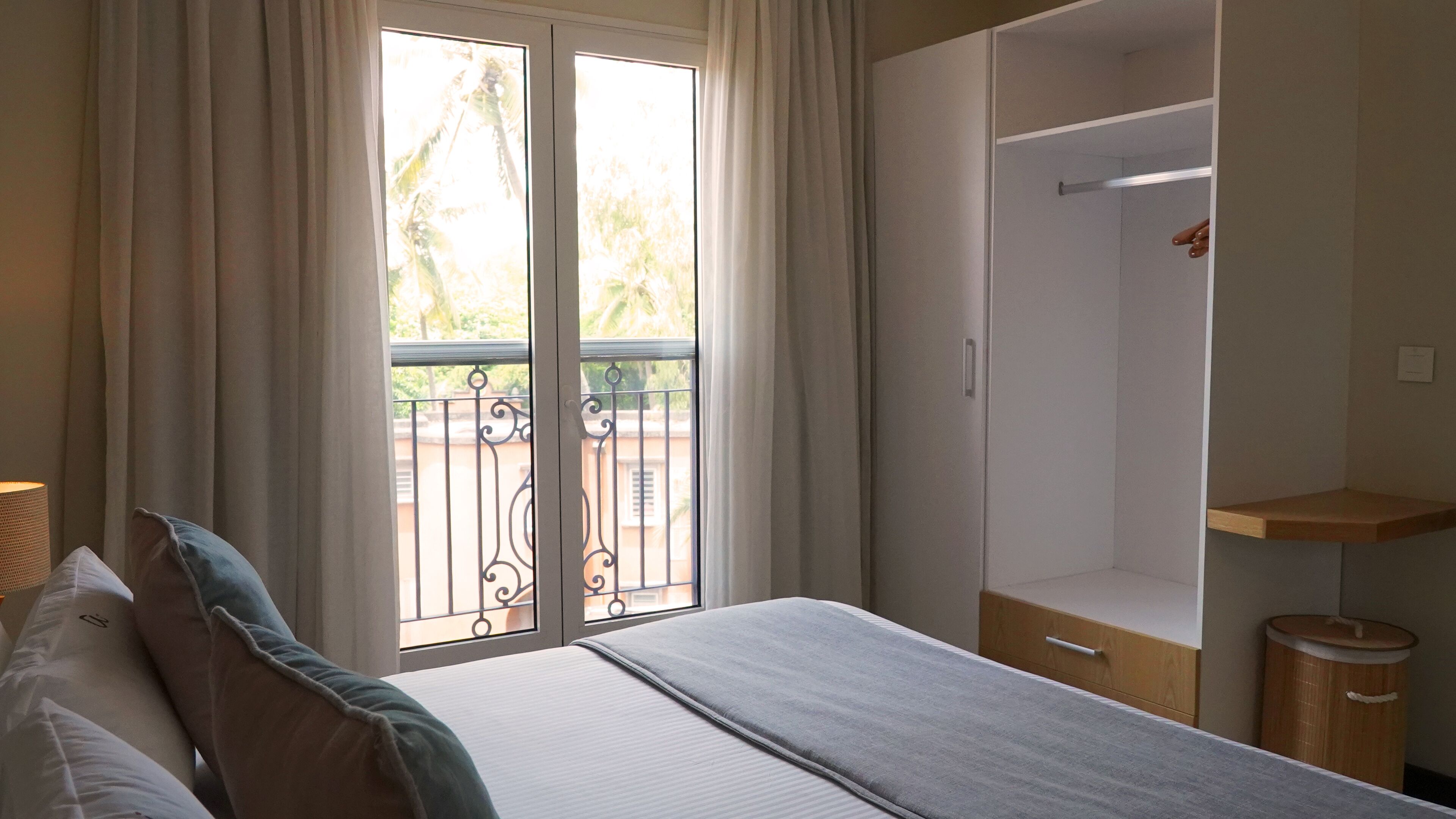 Un dormitorio con cama, armario, una pequeña estantería de madera y un cubo de basura.