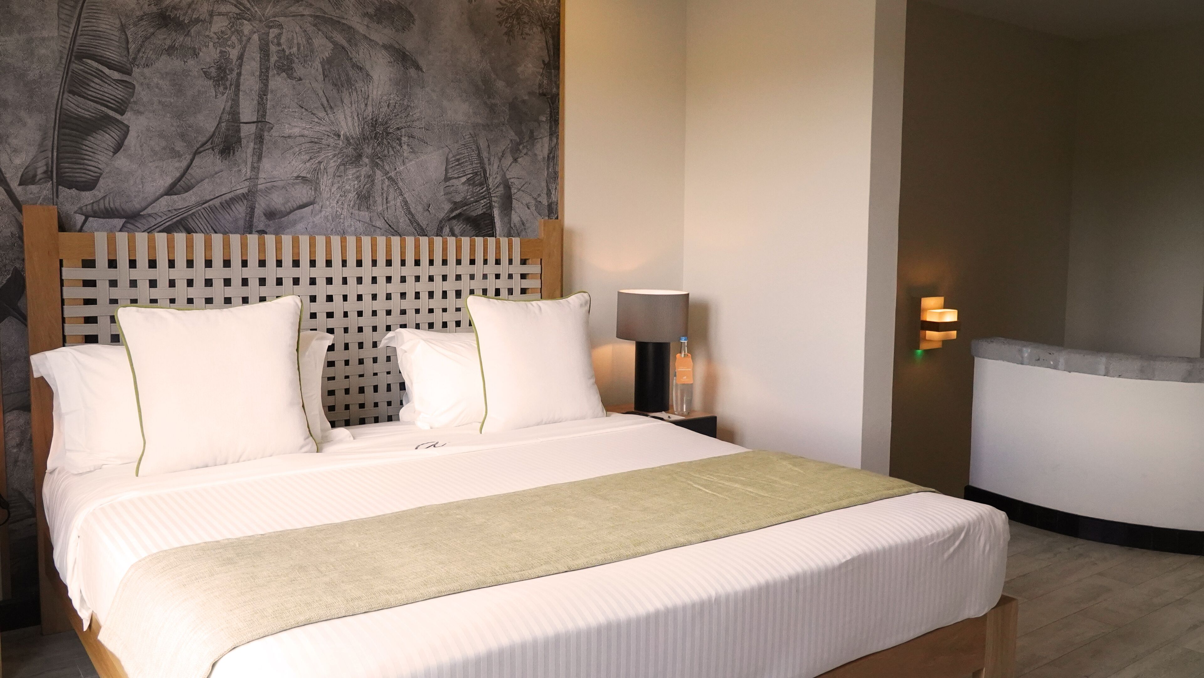 A hotel room with a bed, a nightstand, a lamp, and a wall-mounted light fixture.