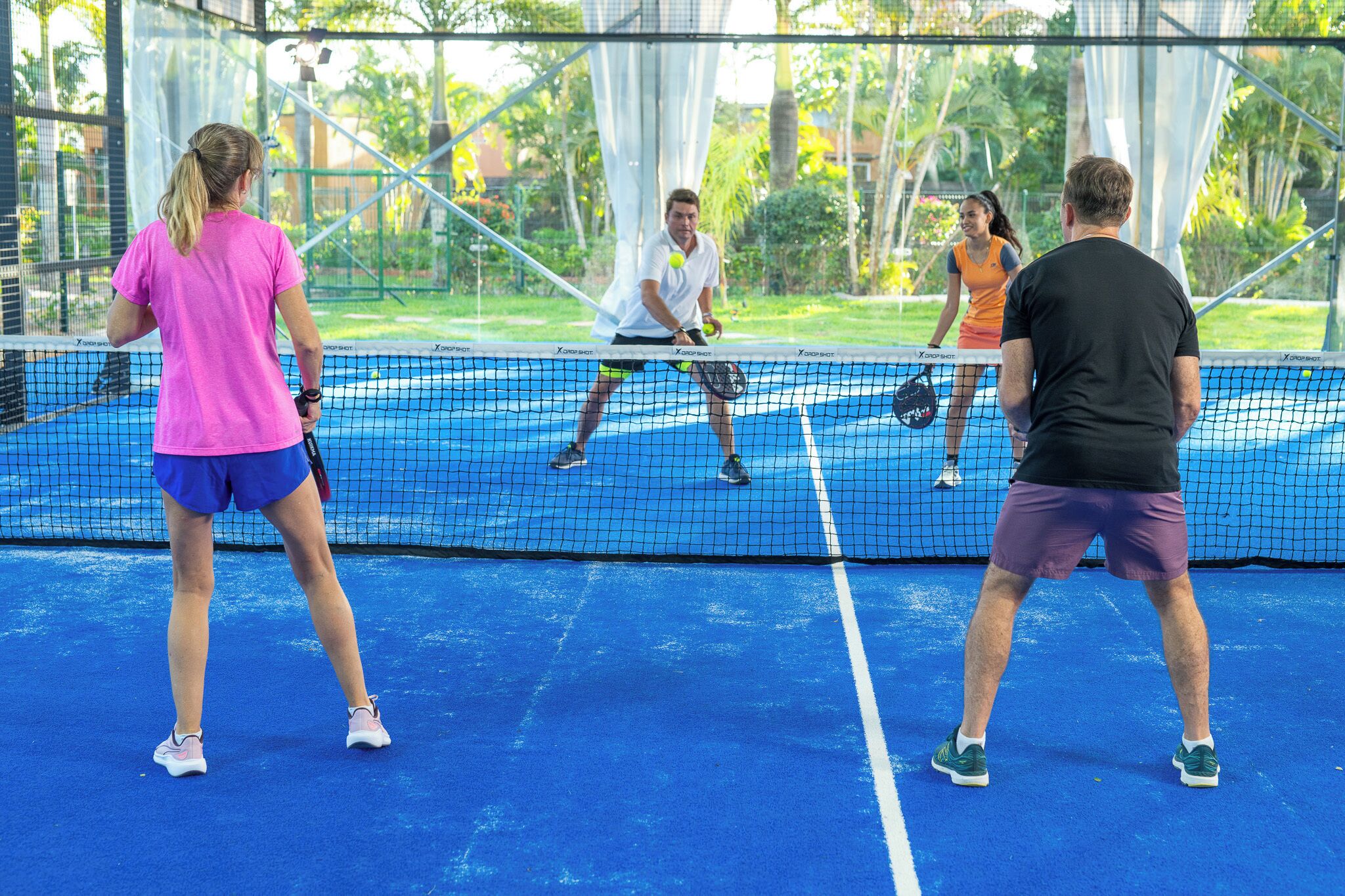 Un court de tennis où des joueurs sont en pleine action, entouré d’un filet et d’une clôture.