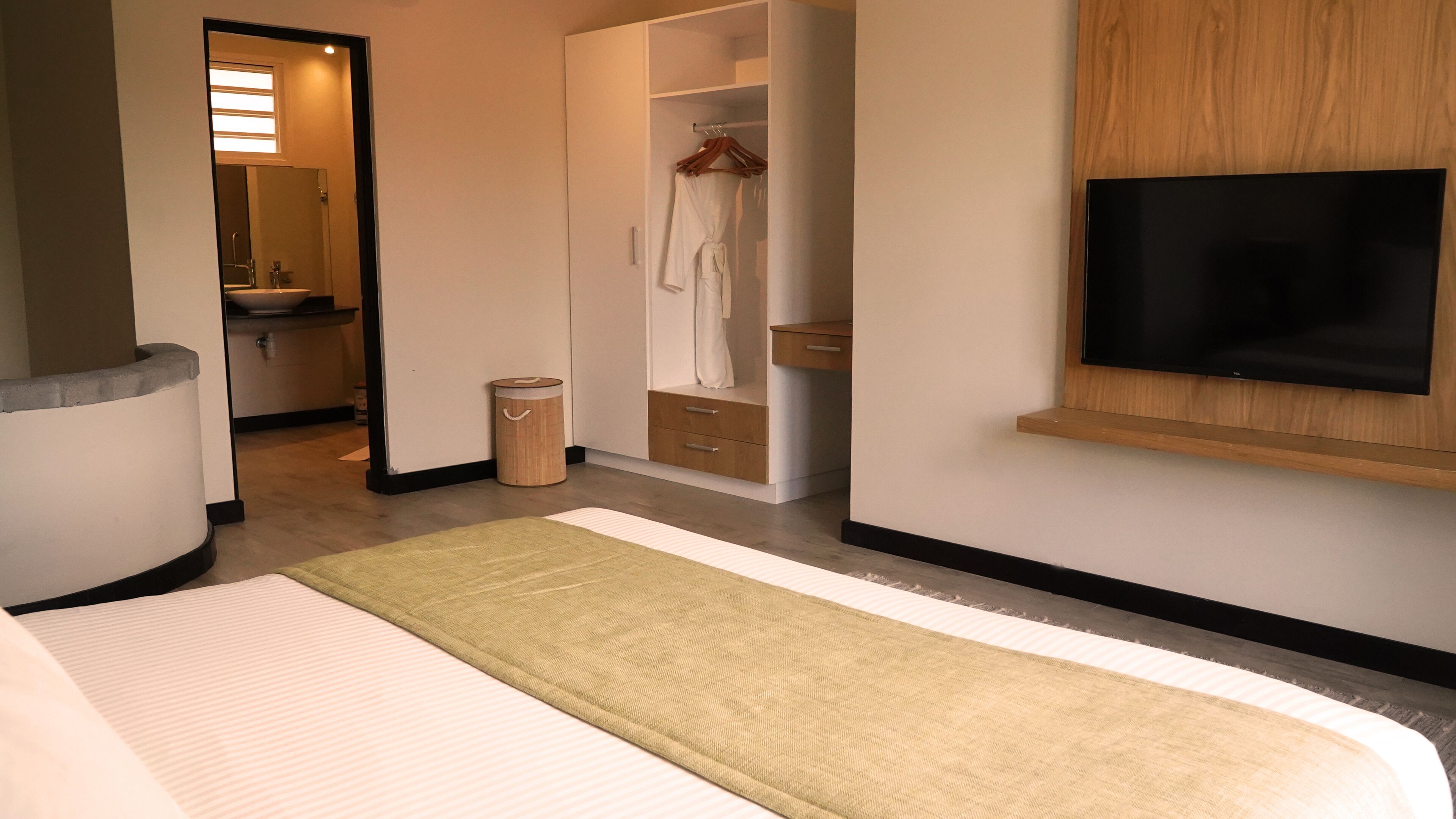 A modern hotel room with a bed, a TV mounted on the wall, a walk-in closet, and a bathroom visible through an open door.